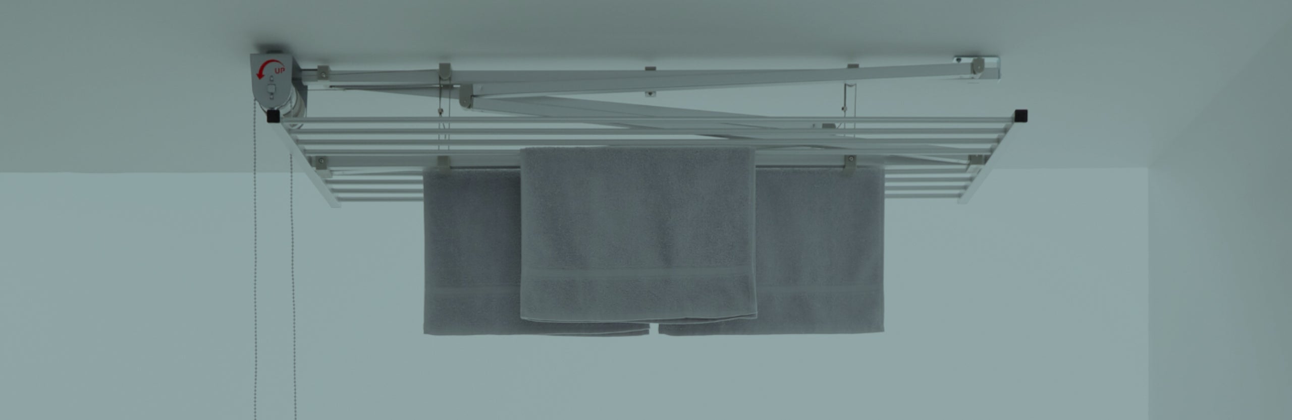 Indoor ceiling mounted clothesline and airer with pulley mechanism for lowering and raising the clothesline. Unit pictured is Foxydry Mini with laundry drying and raised up to the ceiling.